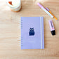 Agenda 2027 de semana vista con portada lila pastel y una ilustración de un gato negro, diseñada y encuadernada a mano.